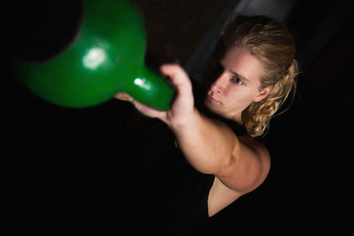 Young woman lifting kettlebell against black background