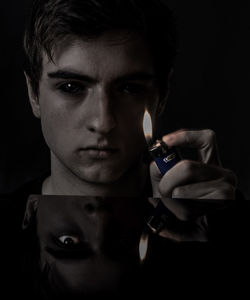Close-up portrait of young man holding cigarette lighter against black background