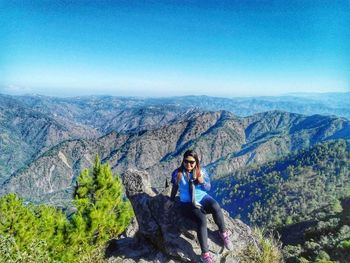 Young woman sitting on rock against mountains