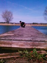 Man sitting on wood by lake against sky