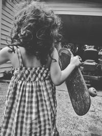 Rear view of girl holding skateboard while standing outdoors