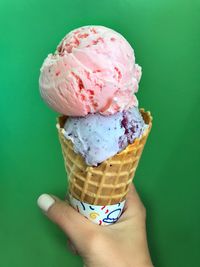 Cropped hand of woman holding ice cream cone against green background