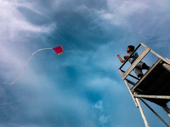 Low angle view of men flying kite against sky