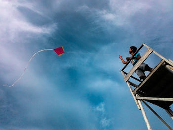 Low angle view of boy flying kite against sky