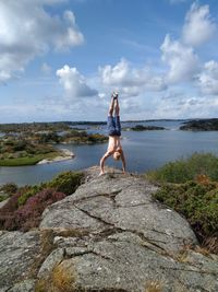 Man standing on rock by sea against sky