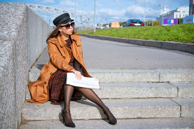 Young woman sits on the steps on the embankment with newspaper in hand