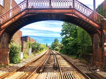 Railroad tracks by bridge against sky