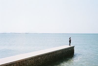 Woman standing on jetty by sea against clear sky
