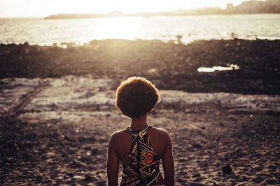 Rear view of woman standing at beach during sunset