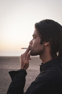Portrait view of man smoking cigarette against clear sky during sunset
