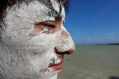 Close-up of man with mud on face against sky