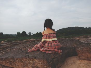 Rear view of woman sitting on land against sky