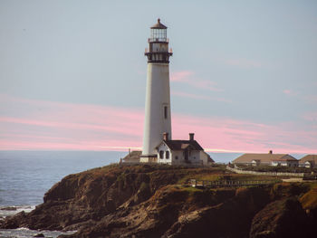 Lighthouse by sea and buildings against sky