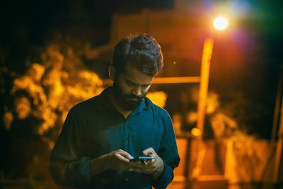 Young man using smart phone on street at night