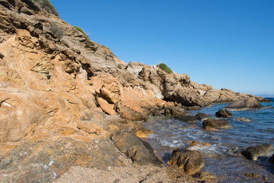 Rock formation in sea against clear blue sky