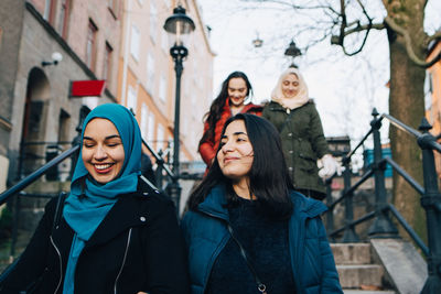 Low angle view of smiling multi-ethnic female friends moving down on staircase in city