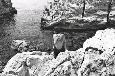 Rear view of woman sitting on rock by sea