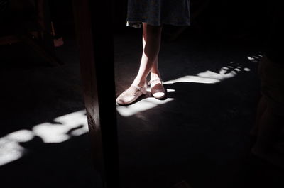 Low section of girl wearing shoes while standing on floor in darkroom