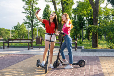 Three young girl friends on the electro scooters taking picture of themselves on cell phone 