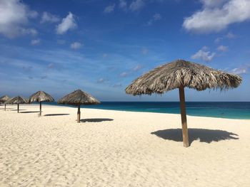 Thatched roof parasols at beach against sky on sunny day