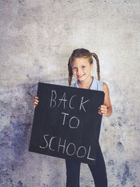 Portrait of smiling girl holding writing slate with text against wall
