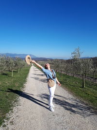 Full length of woman holding hat while standing against sky