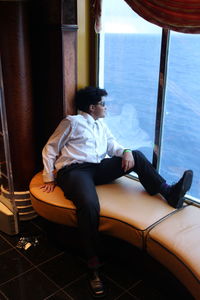 Full length of boy sitting by window in ship