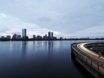 Illuminated bridge over river by buildings against sky in city