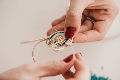 Closeup of crop skilled craftswoman creating soutache bijouterie with threads and beads in bright workshop