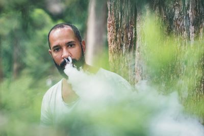 Portrait of mid adult man smoking while standing against tree in forest