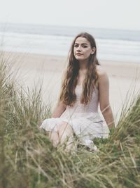 Portrait of young woman sitting on field against sea