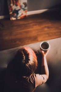 High angle view of girl holding coffee while lying on bed