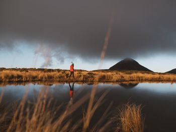 Rear view of man standing by lake against sky