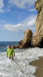 Man on rocks by sea against sky