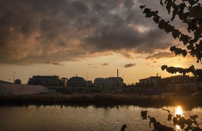 Buildings by lake against sky during sunset