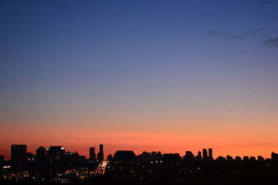 Illuminated cityscape against clear sky during sunset