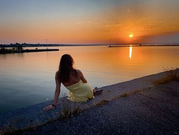 Rear view of woman in yellow dress watching the sun setting over the lake