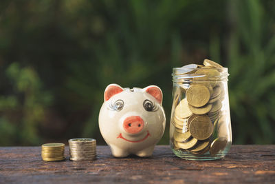 Close-up of coins by piggy bank and jar on table