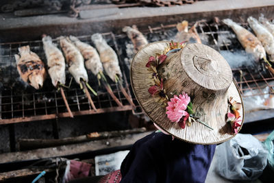 Rear view of woman wearing hat while standing by barbecue grill