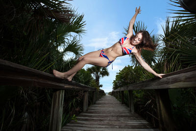 Sensuous woman wearing bikini while balancing on railing at beach