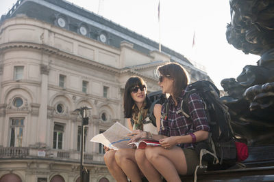 Female backpackers discussing over map while sitting at town square