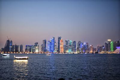 Sea by illuminated buildings against clear sky