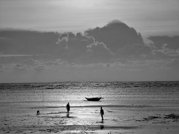 Silhouette men walking at beach against cloudy sky