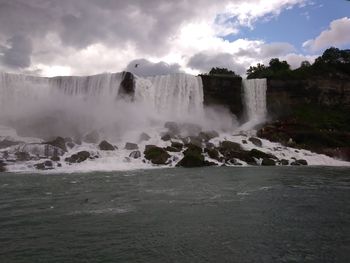 Scenic view of waterfall against cloudy sky