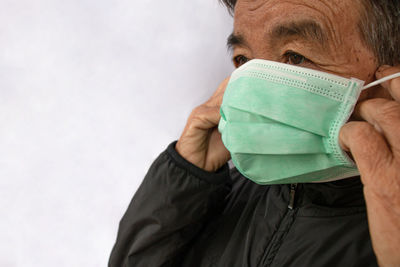 Senior woman putting on mask against white wall