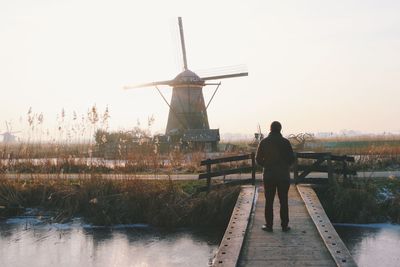 Rear view of man standing on footbridge against sky