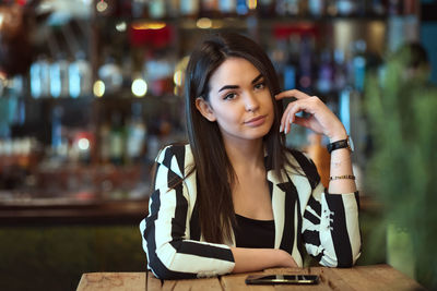 Portrait of young woman using phone while sitting on table