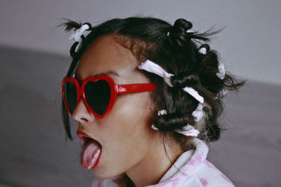 Close-up of woman with tied hair wearing sunglasses while sticking out tongue at home