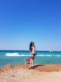 Full length of woman standing at beach against clear blue sky