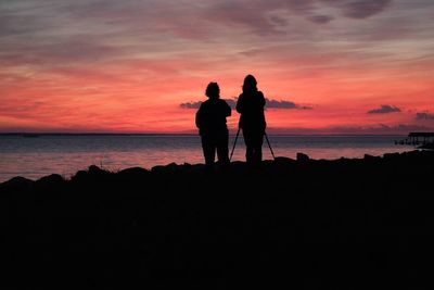 Silhouette of people standing on beach at sunset